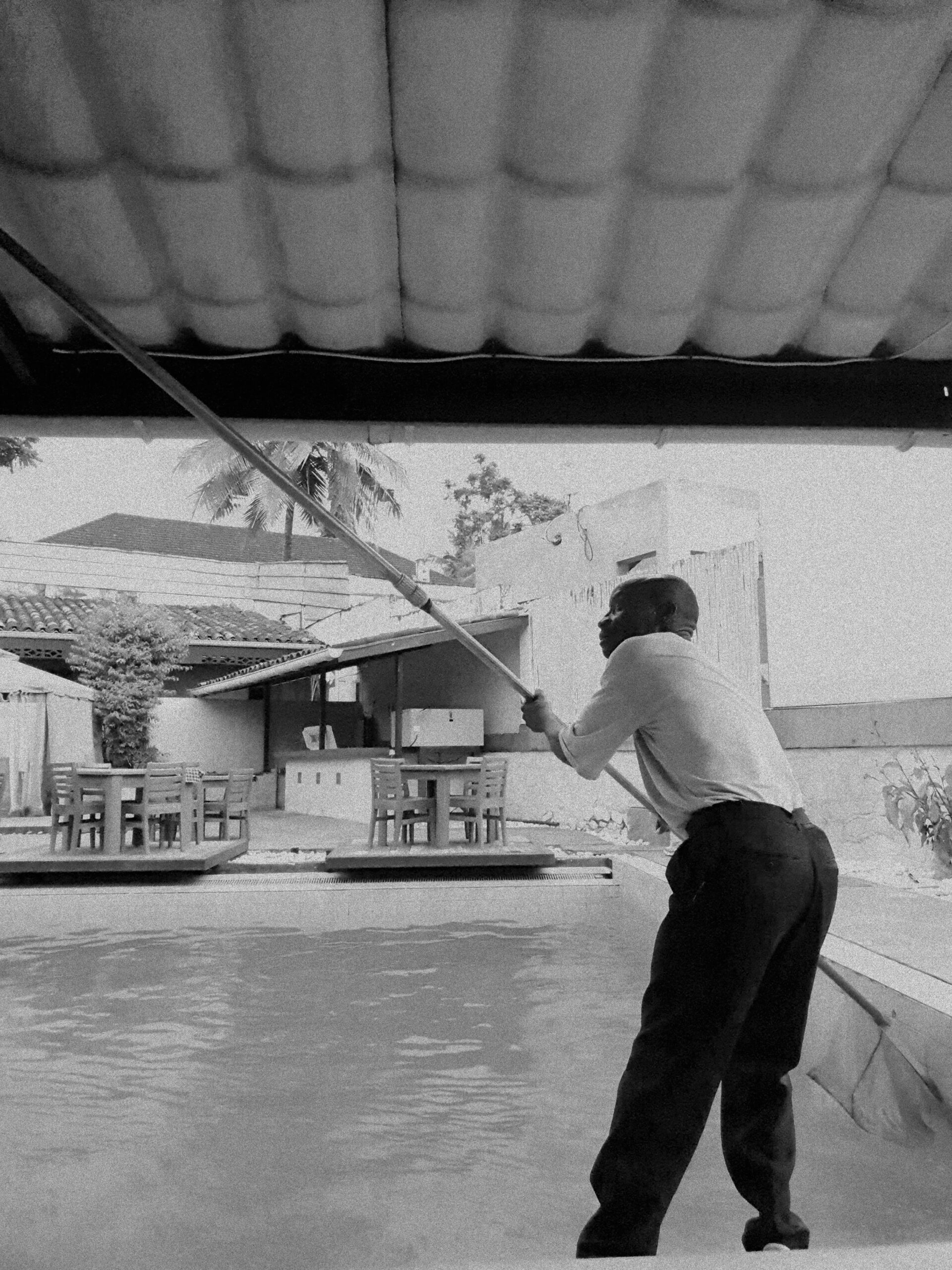 A worker cleaning a pool with a long pole in a covered area.